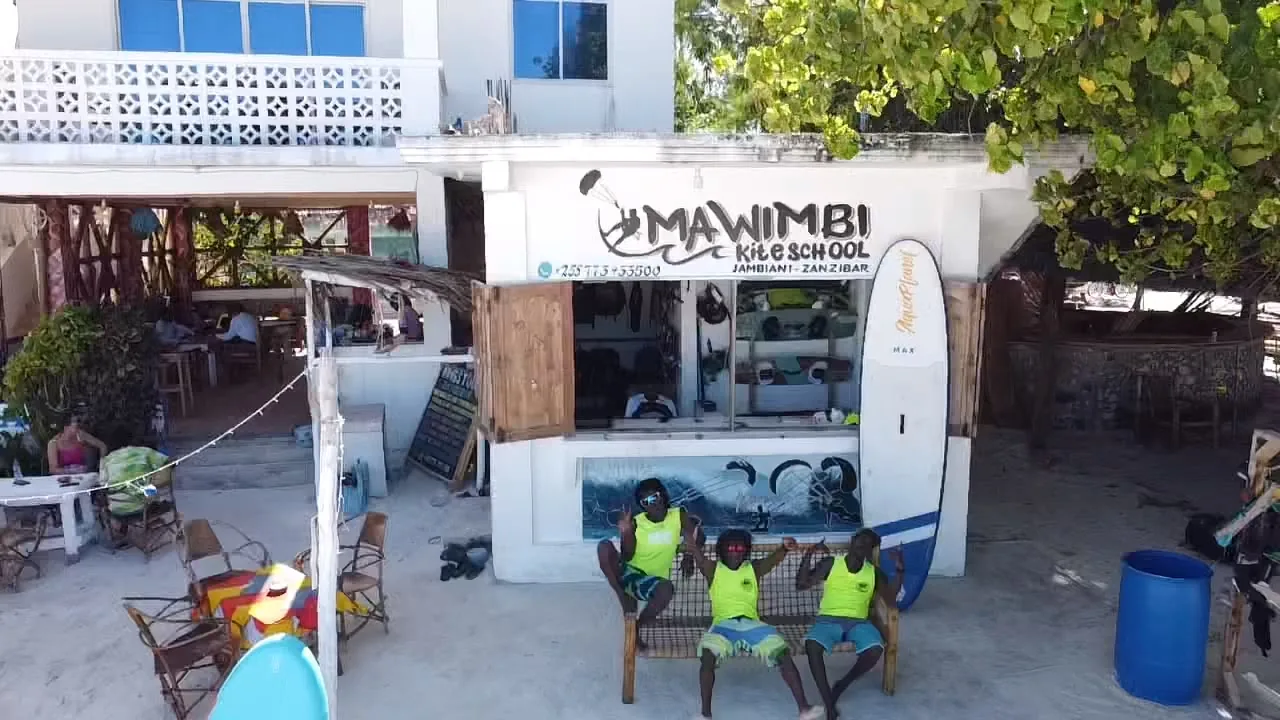 The Mawimbi kite school from above, with its painted sign and the teachers on a bench in front